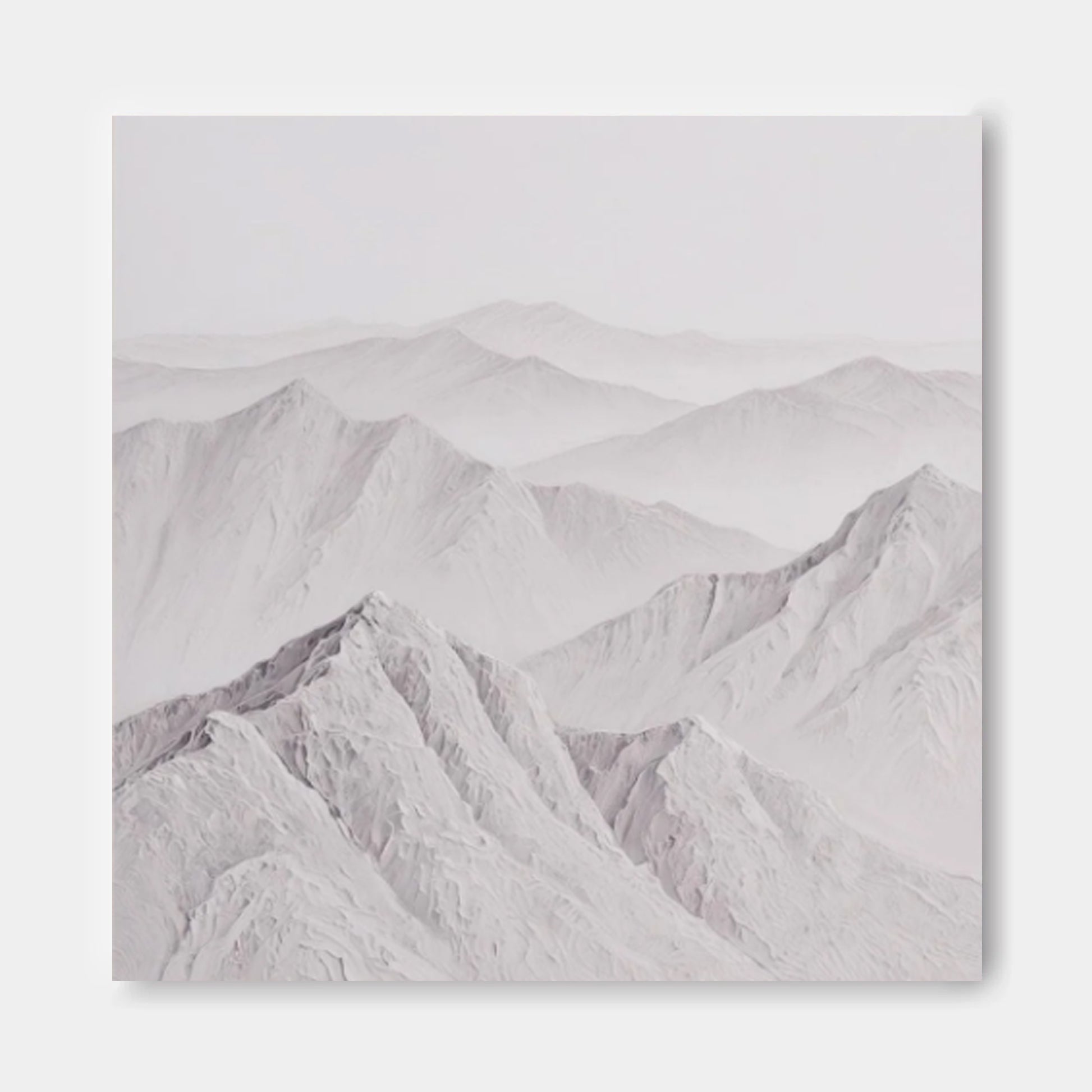 A serene landscape of snow-capped mountains, with their peaks gently rising against a hazy, pale blue sky.