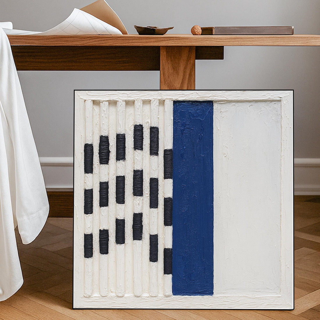 The image is a square-shaped artwork with a white frame, featuring a bold blue vertical line in the center. The artwork is composed of a grid of black and white stripes, creating a striking contrast between the colors.